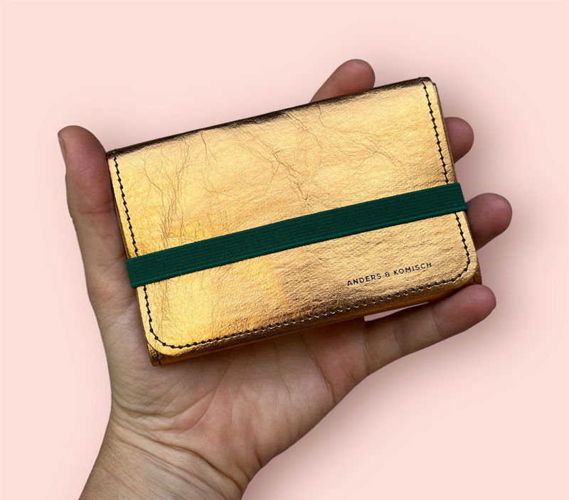 Die A&K KOMPAKT Geldbörse für Damen ist ein Papierportemonnaie in Gold und wird in der Hand gehalten